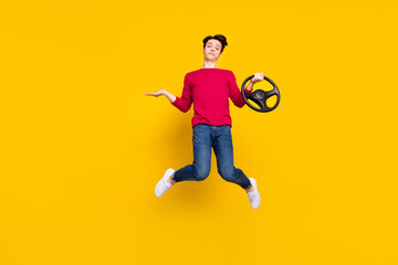 Fototapeta na wymiar Full size photo of unsure brunet young guy jump hold wheel wear red sweater jeans isolated on yellow color background