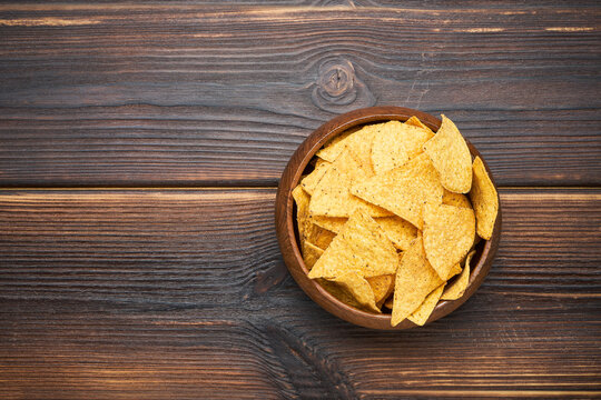 Corn tortilla chips in wooden bowl on a dark background. Flat lay