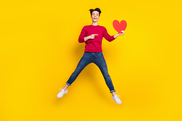 Fototapeta na wymiar Full length photo of excited cute young guy dressed red pullover pointing finger red heart jumping isolated yellow color background