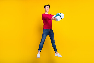 Photo of funny adorable young guy dressed red sweater holding present jumping high isolated yellow color background