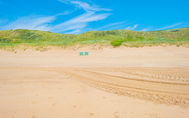 Green grassy dunes along the North Sea coast illuminated by the light of a colorful sun and a blue cloudy sky in summer, Walcheren, Zeeland, the Netherlands, July, 2021