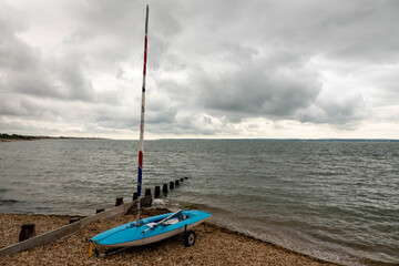 small blue sailing boat on the beach waiting to go out to sea on a stormy summer day