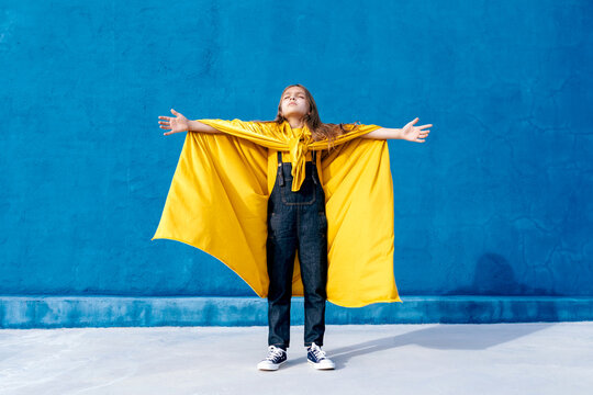 Teenager in cape of superhero on blue background