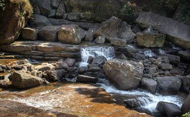 Small natural waterfalls that flow by the mountain rock and the rock boulders.