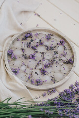 Ice cubes with lavender in glasses standing on a marble tray on wooden background.