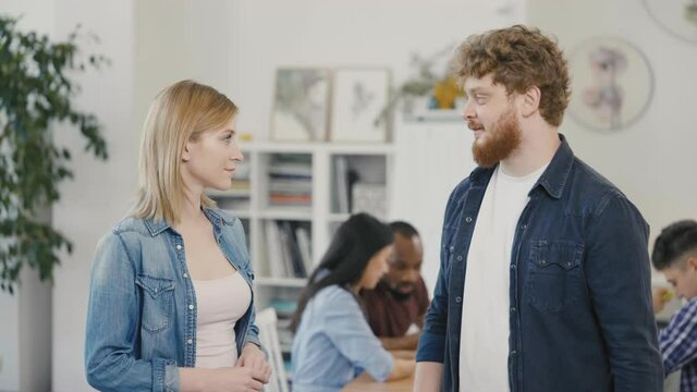 Portrait of a successful young man and woman giving high five during a corporate meeting against the backdrop of a workflow in the office. Slow motion.