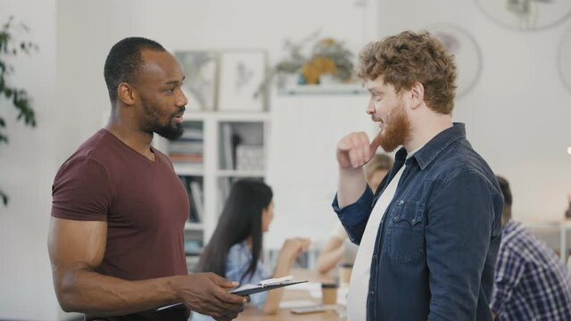 Two colleagues working together discussing teamwork and launching a new startup business project. Men talking, laugh working together at corporate group business meeting. Slow motion.