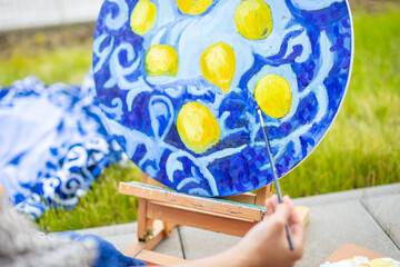 View of hand of young woman painting picture of lemons on blue blanket in home terrace. High quality photo