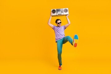 Photo of funny pretty young guy dressed purple t-shirt dark glasses dancing boombox isolated yellow color background