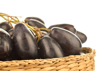 One bunch of black grapes in a straw plate, close-up, isolated on white.