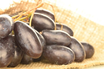 One bunch of ripe black grapes on a jute napkin, close-up, isolated on white.