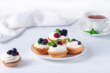 Mini tartlets with whipped cream and fresh berries, on a white table, blurred focus, horizontal, no people,