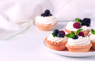 Mini tartlets with whipped cream and fresh berries, on a white table, blurred focus, horizontal, no people,