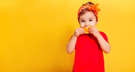 a beautiful little girl in a red T-shirt and an orange bandana eats a slice of orange on a yellow background