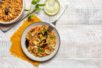 Sardinian lunch. Fregula with seafood on a white wood background. Copy space.
