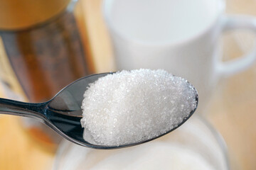 Closeup of spoon of sugar. Spoon of granulated sugar against the background of the white cup and coffee jar. Unhealthy eating concept