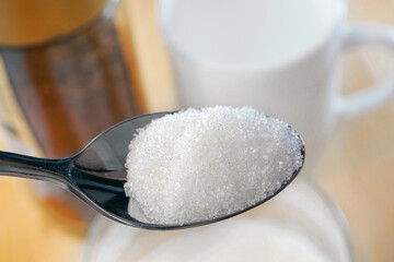 Closeup of spoon of sugar. Spoon of granulated sugar against the background of the white cup and...
