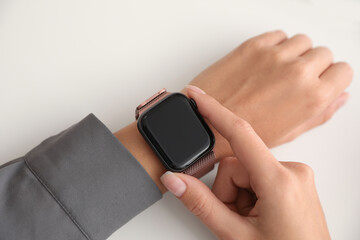 Woman checking stylish smart watch on white background, closeup