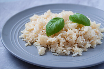 White long rice with basil in a gray plate on a marble background.