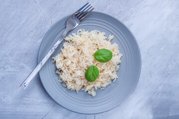 White long rice with basil in a gray plate on a marble background.
