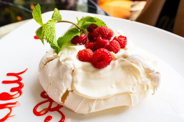 Sweet dessert with berries on a white plate. Meringue with raspberries and syrup.
