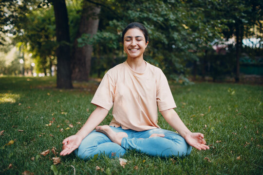 Indian woman doing yoga and meditation in lotus asana pose in outdoor summer park.