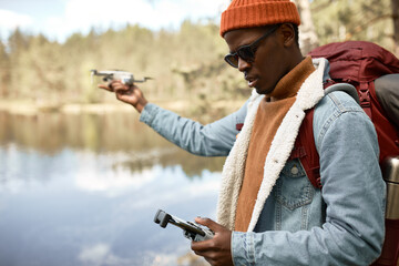 Young aframerican man holding control console for quadcopter. Afro american guy playing with modern gadget in forest. Technology and wild nature connection, travelling concept. Copy space