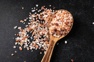 Himalayan pink salt on a black background, in a wooden spoon