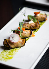 Eggplant rolls with cheese, tomatoes and basil lie on a white plate in a restaurant