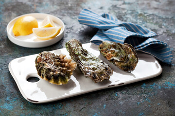 Three closed fresh raw oysters on a white ceramic serving board, selective focus