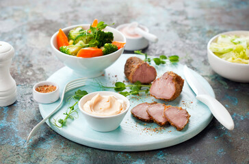 Boiled pork tongue slices with spices, homemade mayonnaise and vegetables on a wooden plate, selective focus