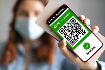 Young girl wearing a face mask holding a passport, ticket pass and smartphone with digital health passport app for travel during covid-19 pandemic.