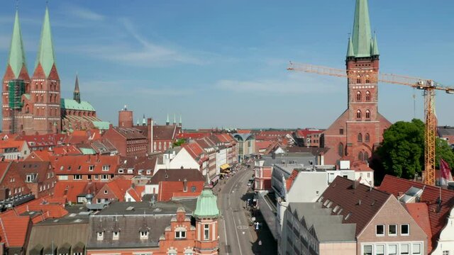 Forwards fly above street in historic town. Aerial view of various buildings along street. Luebeck, Schleswig-Holstein, Germany