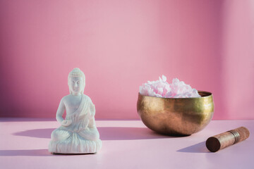 Decorative white Buddha statuette and tibetian singing bowl on pink background. Meditation and...