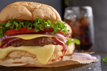 Homemade hamburger or burger with fresh vegetables and cheese lettuce and mayonnaise served, French fries on pieces of brown paper on black stone table . concept of fast food and junk food
