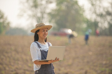 Young happy farmer asia woman standing on field with laptop. A woman farmer examines the farm and sends data to the cloud from the tablet. Smart farming and digital agriculture.
