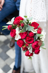 Close up of modern a beautiful and stylish wedding bouquet of red roses and eucalyptus greenery in a bride hands