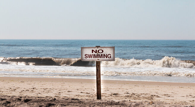 No swimming sign at the beach with waves breaking on the shore