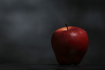 Manzana roja y fresca con gotas de agua sobre mesa negra con fondo negro y espacio para agregar texto. Toma frontal de manzana roja.