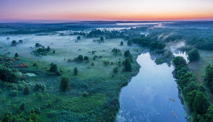 Smoky morning mist over the river. Beautiful panoramic view of river and green banks of the river in the early summer morning.