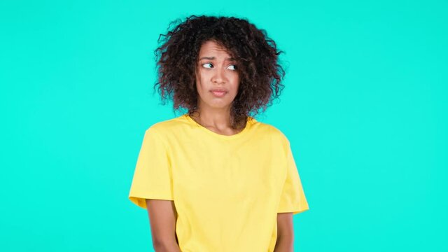 Guilty confused african woman making oops, im sorry expression. Girl with curly hair is ashamed and feeling uncomfortable because of guilt. Teal studio background