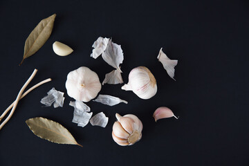 
Garlic with spices and bay leaf on a black background, top view. Food background.