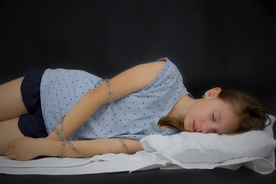 The little girl is lying in bed. She is chained.The sleeping girl is wrapped in a chain.