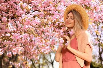 Happy stylish young woman near blossoming sakura tree outdoors. Spring look