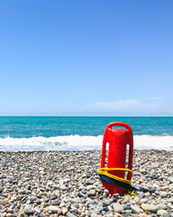Red rescue float on rocky beach with sea panorama and no lifeguard. Static blank space copypaste...