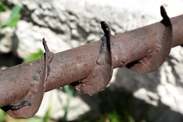 A rusty deformed auger closeup, located on a concrete slab with a blurry background on a sunny day