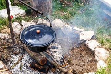 Metal cauldron boiling on a bonfire. Cooking on open fire, camping meal. Traditional preparation of...