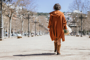 Young woman with poncho and a bouquet of flowers in her hand walking. Close up.