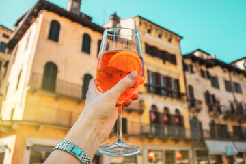 Female hand with glass of orange cocktail spritz on the background of old buildings. Alcoholic...