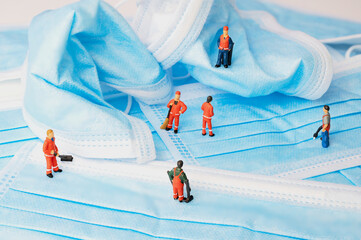Miniature men of the waste disposal standing in front of blue medical masks, symbolic for the masks...